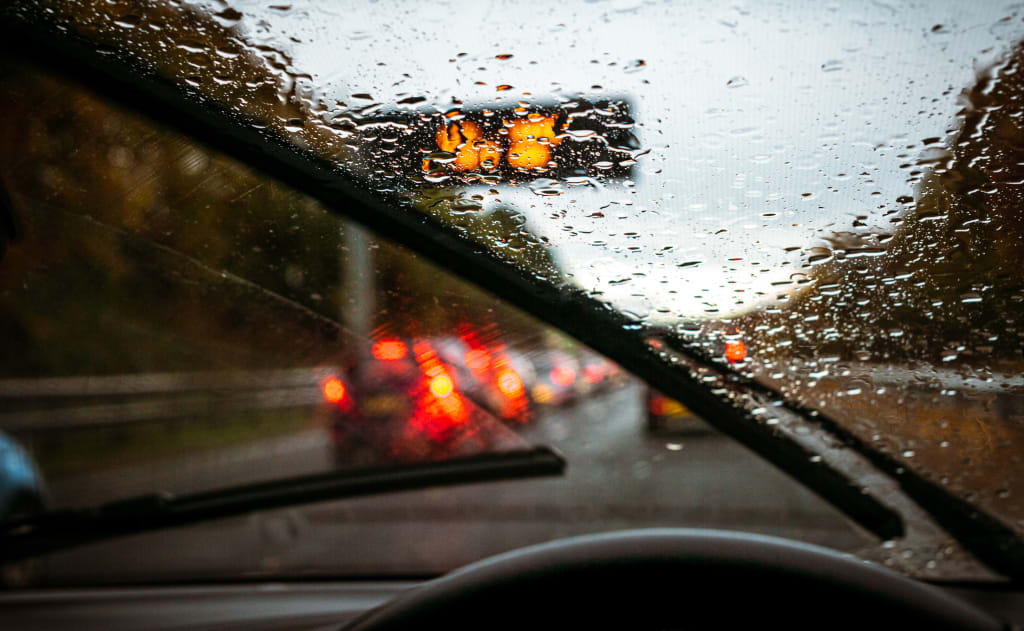Car driving on a busy motorway in wet weather, working windscreen wipers visible.